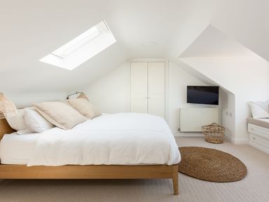 A bedroom with a wooden bed frame white bedding beige pillows a skylight built in wardrobe a wall mounted tv and a woven round rug at Beach Haven in West Bexington