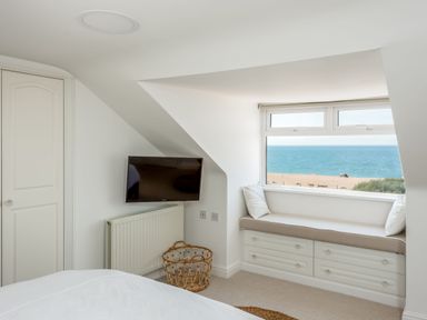 A bedroom with a wall-mounted television a window seat with cushions and a view of the sea at Beach Haven in West Bexington