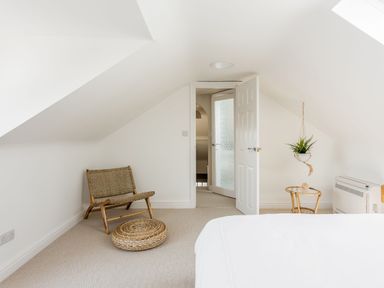 A bedroom with a chair a round cushion a small table with a hanging plant and an open door at Beach Haven in West Bexington