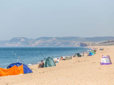 A beach with people fishing tents and chairs along the shoreline at Beach Haven in West Bexington