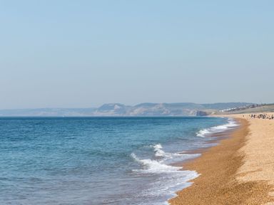 A beach with waves and sand and distant hills at Beach Haven in West Bexington