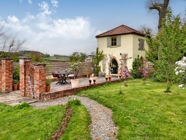 A small two-story building with a tiled roof surrounded by a garden and a gravel path at The Folly in Weobley