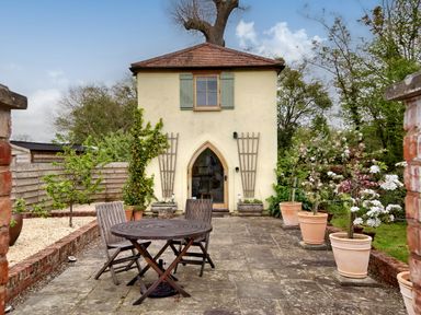 A garden patio with wooden chairs and table in front of a small building with a tiled roof at The Folly in Weobley
