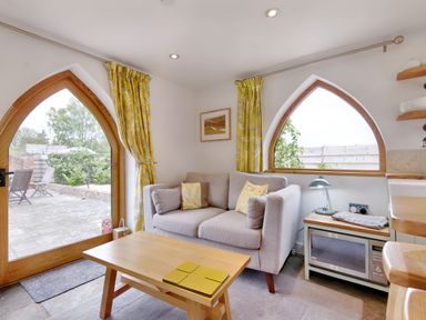 A small living area with a gray sofa yellow cushions wooden coffee table microwave and arched windows with yellow curtains at The Folly in Weobley