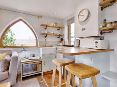 A kitchen area with wooden shelves and stools and a large arched window at The Folly in Weobley