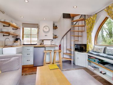 A kitchen and living area with spiral staircase wooden stools and built in seating with cushions at The Folly in Weobley