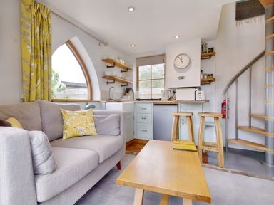 A small living area with a sofa, coffee table, kitchen with appliances, open shelves, and a spiral staircase at The Folly in Weobley