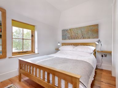 A bedroom with a wooden bed frame white bedding lamps and a window with a yellow blind at The Folly in Weobley