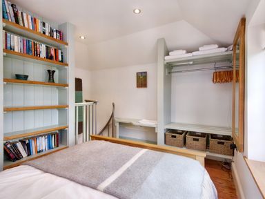 A bedroom with a bed a bookshelf with books open closet with baskets and hangers and a small desk at The Folly in Weobley