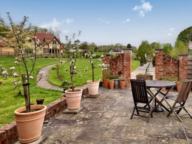 A garden patio with potted plants a round wooden table and chairs and a gravel path leading to a house at The Folly in Weobley