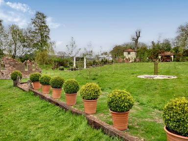 A garden with potted shrubs lined on a raised border and garden ornaments at The Folly in Weobley