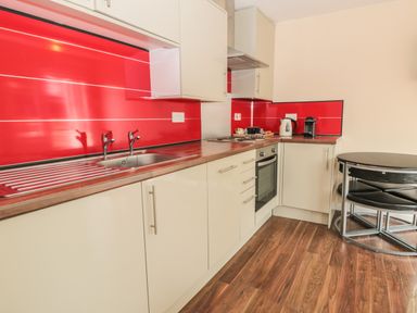 A kitchen with beige cabinets red backsplash stainless steel sink and stove and a black round table with chairs at Vallum Kiosk in Haltwhistle
