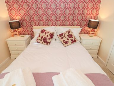 A bedroom with a double bed white bedding two floral pillows two bedside tables each with a lamp against a red patterned wallpaper at Vallum Kiosk in Haltwhistle