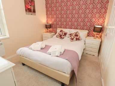A bedroom with a double bed white bedding and purple accents two bedside tables with lamps and floral wallpaper at Vallum Kiosk in Haltwhistle