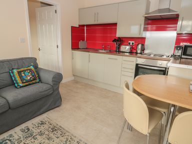 A kitchen with white cabinets red backsplash a gray sofa and a wooden dining table with cream chairs at Vallum Kiosk in Haltwhistle