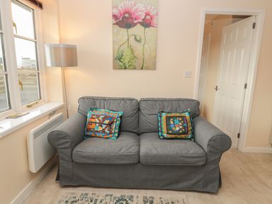 A gray sofa with two colorful cushions under a floral painting beside a window with a floor lamp at Vallum Kiosk in Haltwhistle
