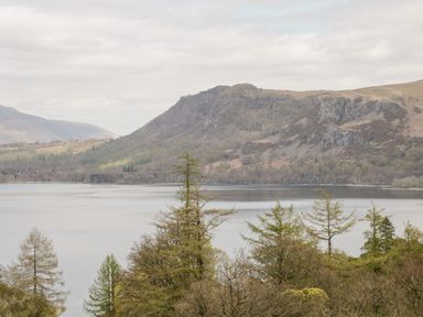 A lake with trees in the foreground and hills in the background at Holly Cottage in Keswick
