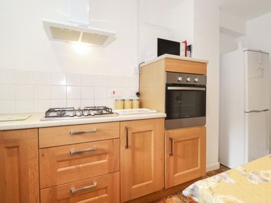 A kitchen with wooden cabinets a gas stove an oven a microwave and a white refrigerator at Holly Cottage in Keswick