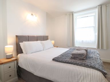 A bedroom with a bed with striped bedding bedside tables with lamps and a window with curtains at Holly Cottage Keswick