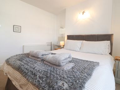 A bedroom with a bed with striped pillows and folded towels on a grey blanket at Holly Cottage in Keswick