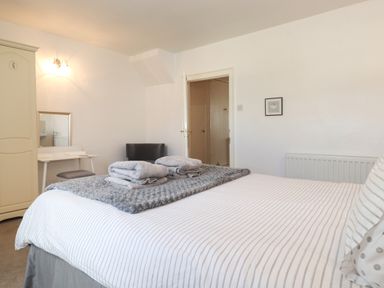 A bedroom with a bed with folded towels on a blanket a wardrobe a chair a dressing table and a door at Holly Cottage in Keswick