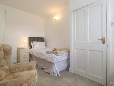 A bedroom with a single bed side table lamp armchair and a closed door at Holly Cottage in Keswick