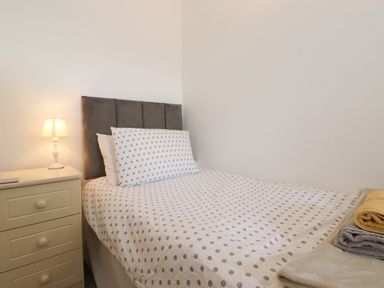 A bedroom with a single bed with polka dot bedding a bedside table with a lamp and folded towels at Holly Cottage in Keswick