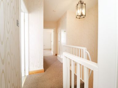 A carpeted hallway with wallpaper and a white staircase railing at Holly Cottage in Keswick