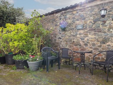 An outdoor seating area with plastic chairs a small round table and potted plants against a stone wall at Holly Cottage in Keswick