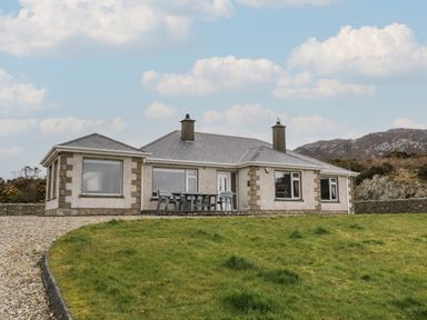 A single story house with large windows a gravel driveway and a patio table with chairs on the side at Ranny Roe in Portsalon County Donegal