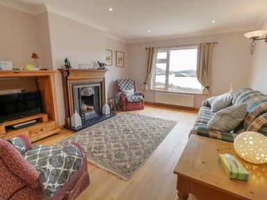 A living room with armchairs a fireplace a television a sofa and a window overlooking water at Ranny Roe in Portsalon County Donegal