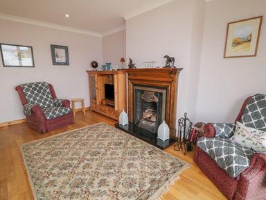 A living room with two armchairs a fireplace a wooden cabinet and a patterned rug on the floor at Ranny Roe in Portsalon County Donegal
