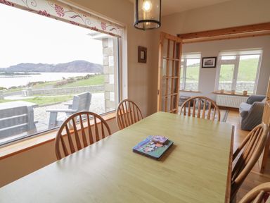 A dining area with a wooden table and chairs next to large windows showing an outdoor seating area and a view of hills at Ranny Roe in Portsalon County Donegal