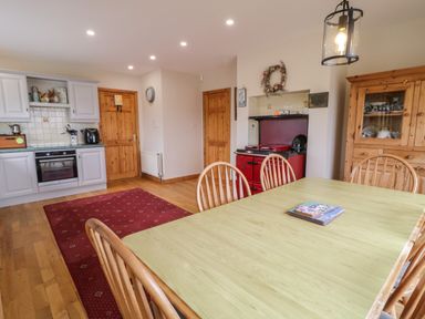 A kitchen dining area with a wooden table and chairs a red rug a red stove and wooden cabinets at Ranny Roe in Portsalon County Donegal