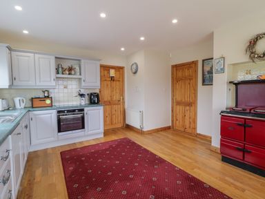 A kitchen with white cabinets a red stove wooden doors and a red rug on the floor at Ranny Roe in Portsalon County Donegal
