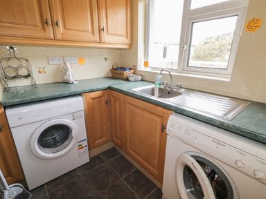 A kitchen corner with wooden cabinets a sink two front load washers and a window at Ranny Roe in Portsalon County Donegal