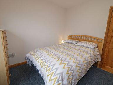 A bedroom with a double bed with patterned bedding a wooden door and a chest of drawers at Ranny Roe in Portsalon County Donegal