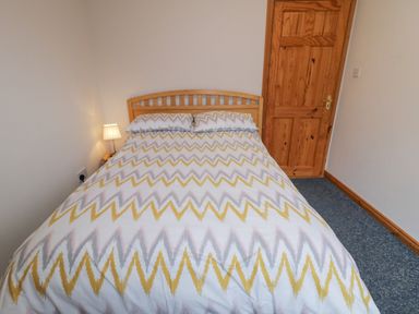 A bedroom with a double bed wooden door and bedside lamp at Ranny Roe in Portsalon County Donegal
