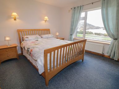 A bedroom with a wooden bed and two nightstands with lamps next to a window with curtains at Ranny Roe in Portsalon County Donegal