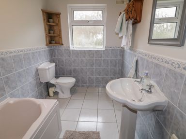 A bathroom with a bathtub toilet sink tiled walls and floor with a small wooden shelf on the wall at Ranny Roe in Portsalon County Donegal