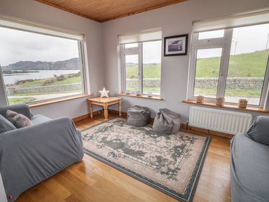 A seating area with two armchairs a corner table two bean bags and large windows overlooking a lake and green fields at Ranny Roe in Portsalon County Donegal