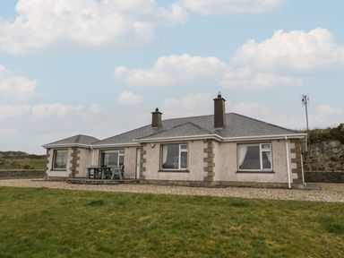 A single story house with two chimneys and windows on a grassy area at Ranny Roe in Portsalon County Donegal
