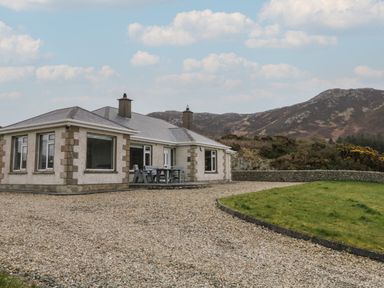 A single story house with a gravel driveway a grass lawn and mountains in the background at Ranny Roe in Portsalon County Donegal