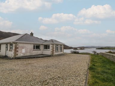 A single-story house with a gravel driveway next to a body of water at Ranny Roe in Portsalon County Donegal