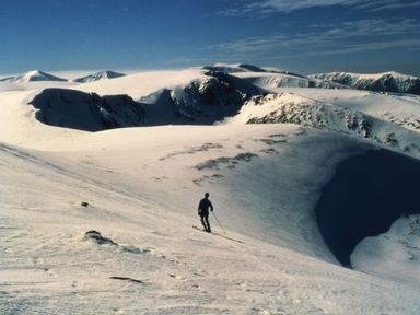 A person skiing on a snowy mountain slope with snow covered peaks in the background at Otter Lodge in Feshiebridge near Aviemore