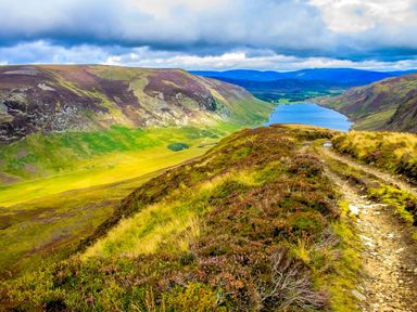 A mountain landscape with a narrow dirt path beside a lake surrounded by hills at Otter Lodge in Feshiebridge near Aviemore