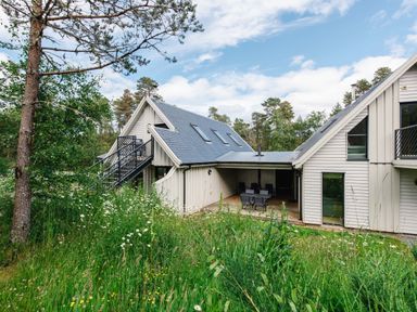A house with grey roof and white walls surrounded by trees and tall grass at Otter Lodge in Feshiebridge near Aviemore