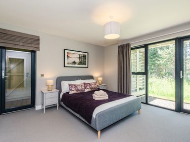 A bedroom with a double bed between two bedside tables and large windows showing grass at Otter Lodge in Feshiebridge near Aviemore
