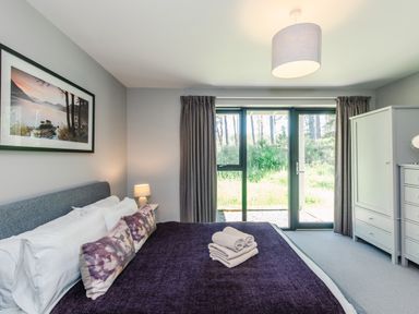 A bedroom with a bed with pillows and towels a lamp a wardrobe and a glass door looking outside at Otter Lodge in Feshiebridge near Aviemore