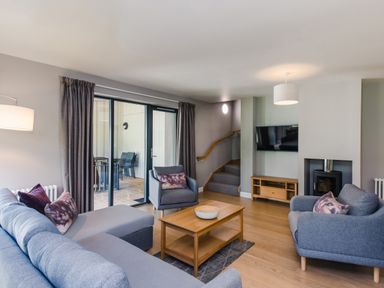 A living room with blue sofa chairs a wooden coffee table and a wall-mounted TV at Otter Lodge in Feshiebridge near Aviemore